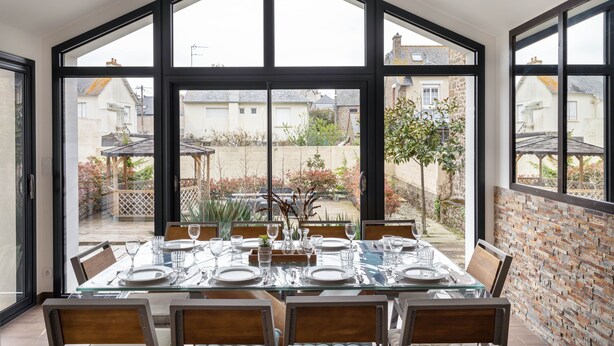 Ein Essbereich mit großem Tisch für sechs Personen, großen Fenstern und Blick auf den Garten.