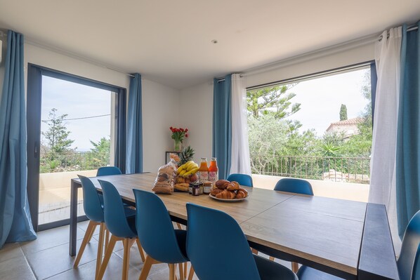 A dining area with a table set for four, blue chairs, and a variety of food items including bread, fruits, and pastries.