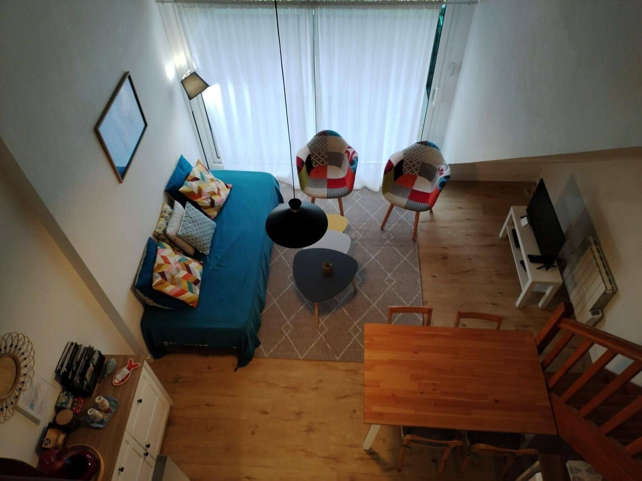 A room with a bed, a dining table, and two chairs. There is a TV on a stand and a lamp on the wall.