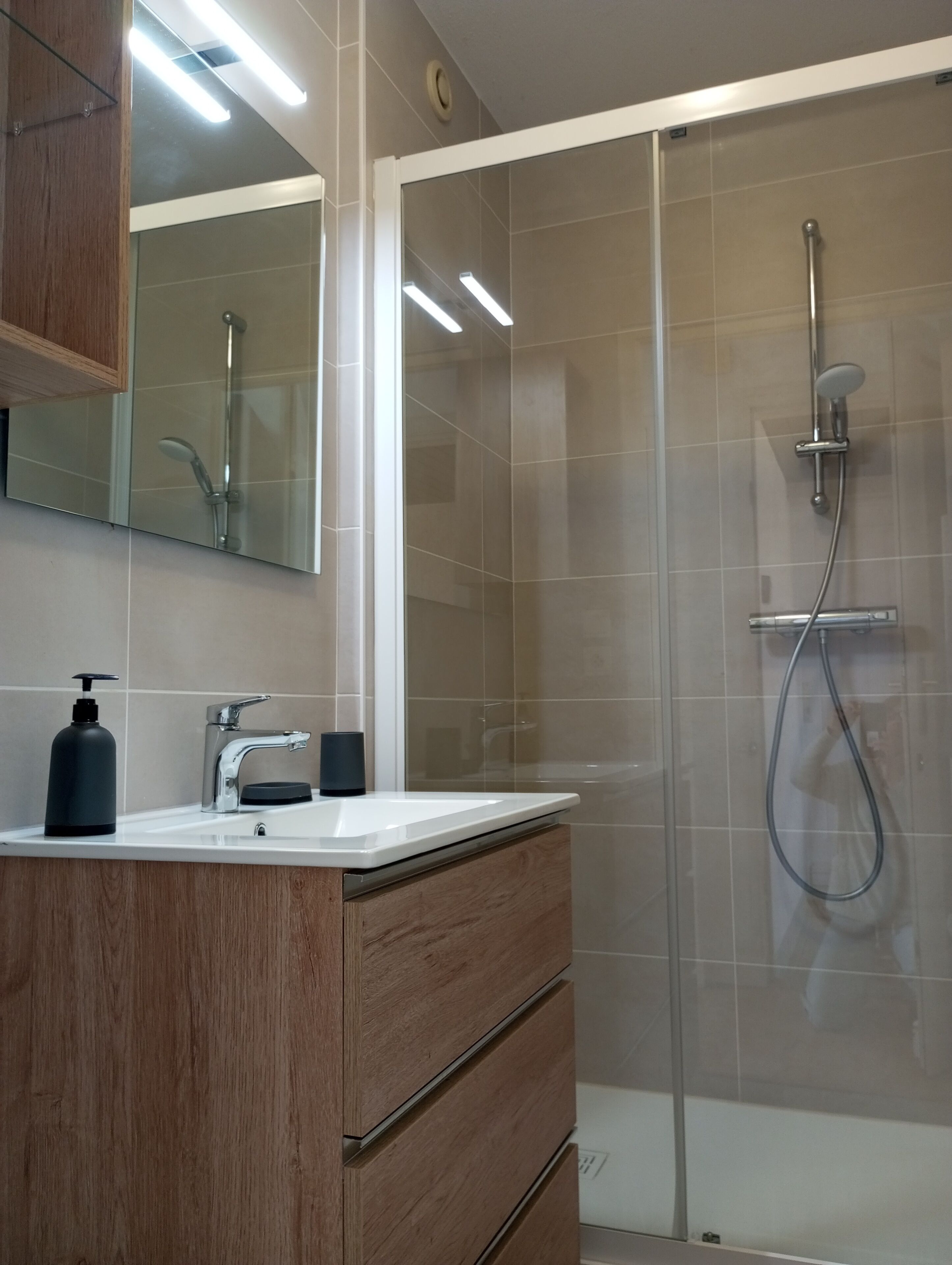 A modern bathroom with a glass-enclosed shower, a wooden vanity with a mirror, and a white sink.
