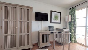 Ein Zimmer mit einem Bett, einem Schreibtisch mit Laptop, einem Fernseher, einer gerahmten Pflanze und einem Kleiderschrank.