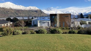 Un bâtiment moderne à la façade en pierre et aux grandes fenêtres, entouré d’une pelouse bien entretenue et offrant une vue sur des montagnes aux sommets enneigés.