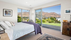 Une chambre avec un grand lit, une vue sur les montagnes et une porte-fenêtre coulissante donnant sur un balcon.