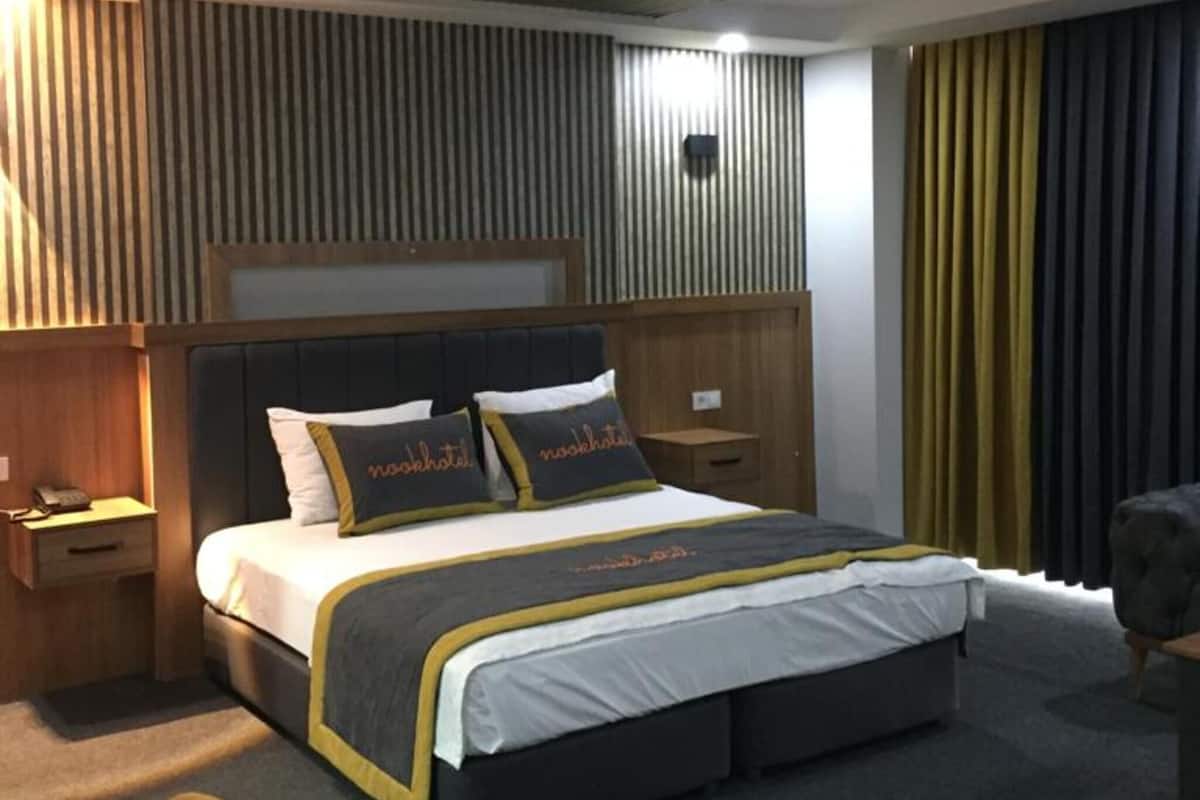 A modern hotel room with a large bed, a bedside table, a chair, and a unique ceiling design.