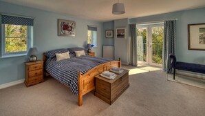 Une chambre avec un lit en bois, une table de chevet, un banc et une vue sur l’extérieur grâce à une porte vitrée.