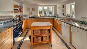 Une cuisine moderne dotée d’un îlot central, de meubles en bois, d’une cuisinière en acier inoxydable et d’une fenêtre laissant entrer la lumière naturelle.