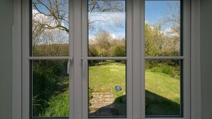 Une fenêtre à trois vitres, chacune offrant une vue sur un espace extérieur verdoyant, avec des arbres et un ciel dégagé.