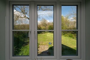 Ventana de tres paneles, cada uno con vista a un área verde exterior con árboles y cielo despejado.