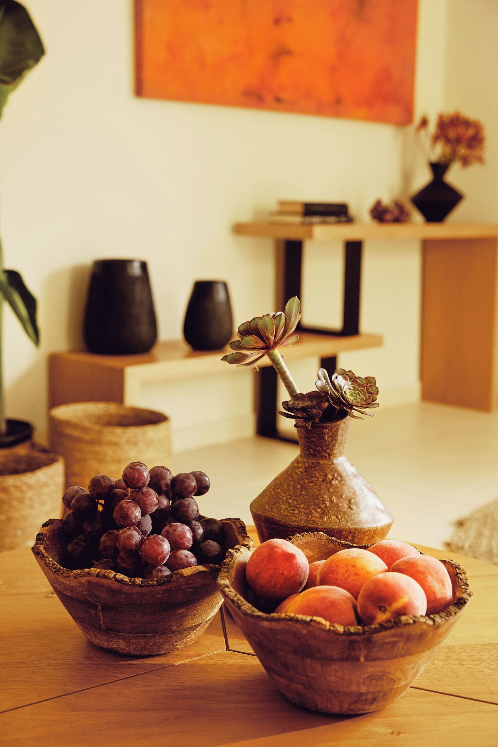 Une table en bois sur laquelle sont posés deux bols remplis de fruits et un vase contenant des plantes succulentes.