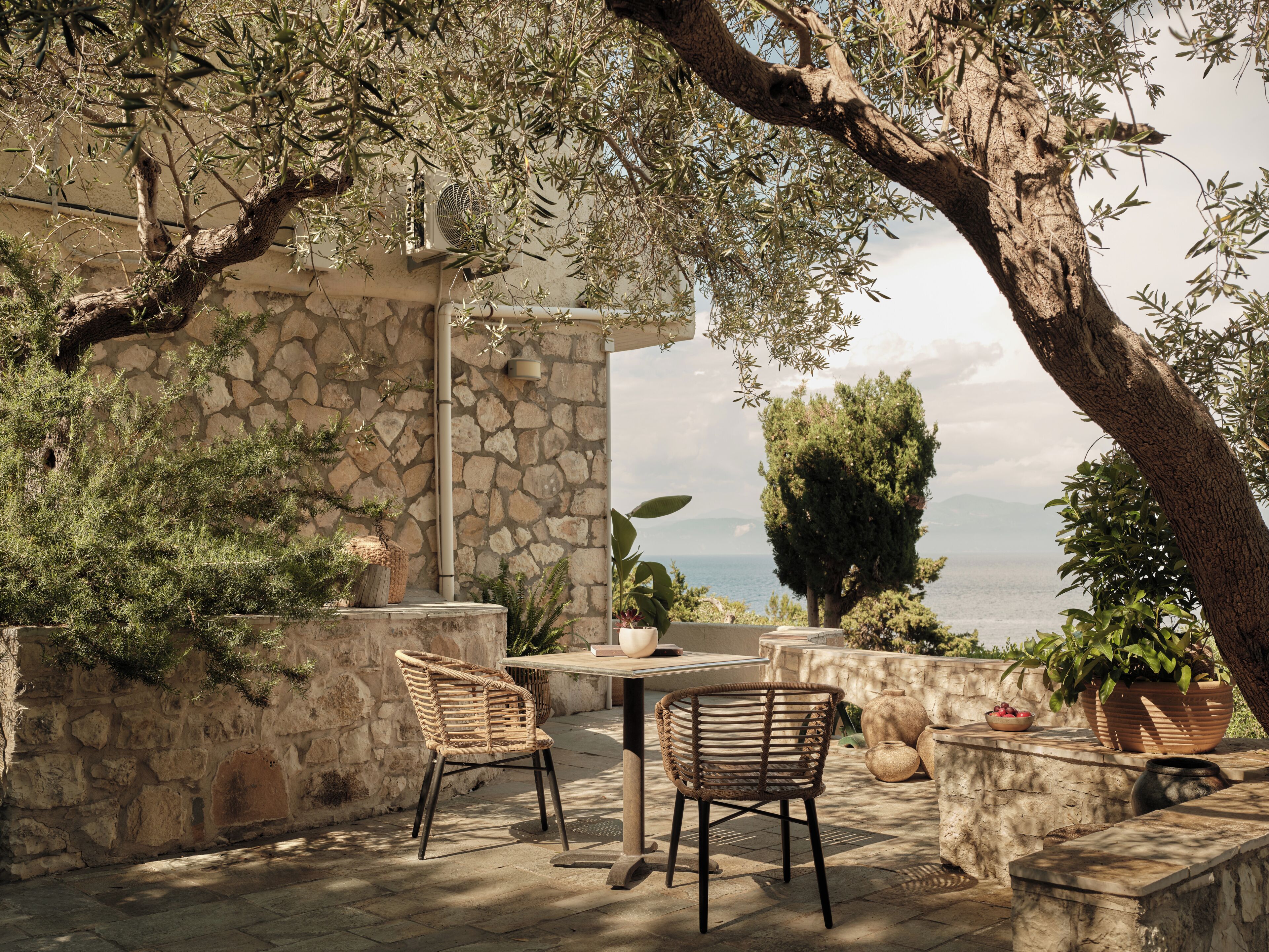 Une terrasse extérieure avec des murs en pierre, une table, deux chaises en osier et des plantes en pot.