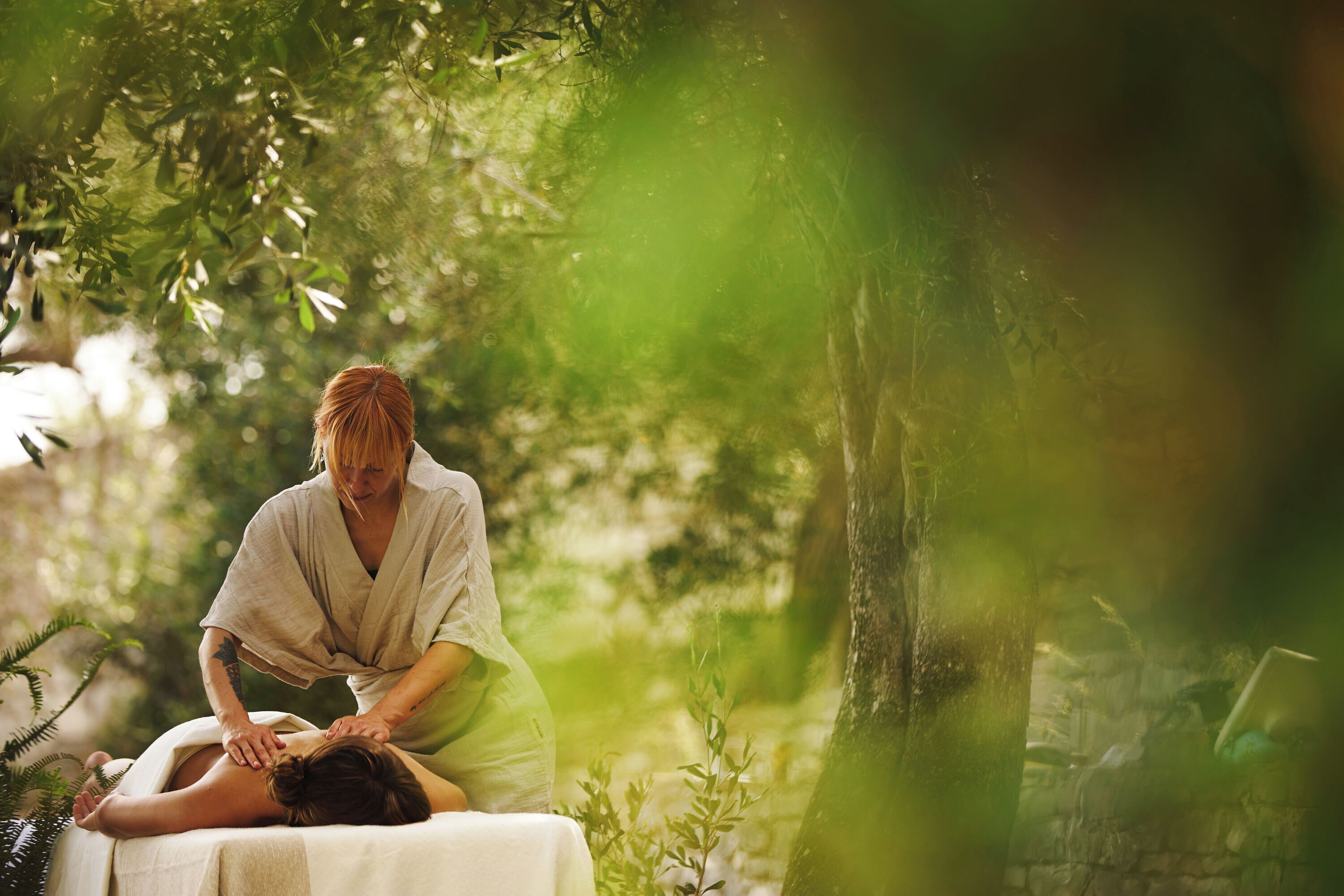 Une personne reçoit un massage en plein air, avec une végétation luxuriante et des arbres en arrière-plan.