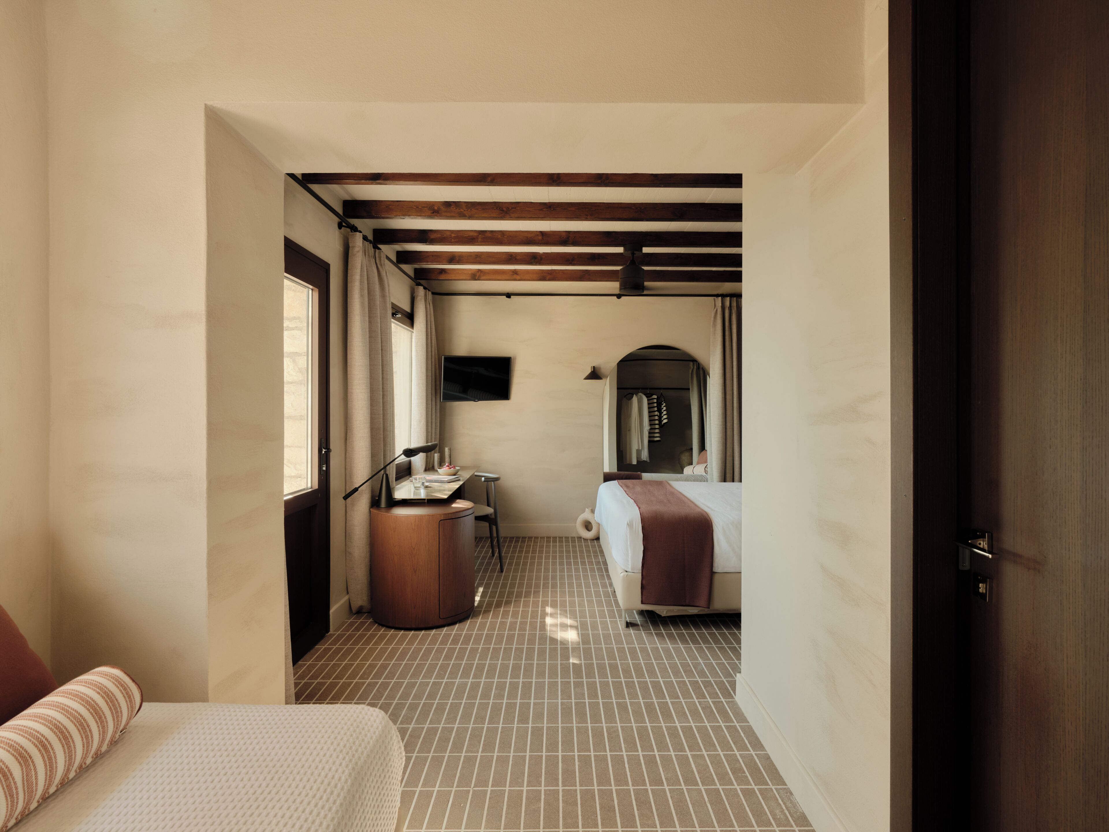 Una camera d'albergo con un letto, una scrivania con una sedia, una televisione e un bagno visibile tramite un arco.