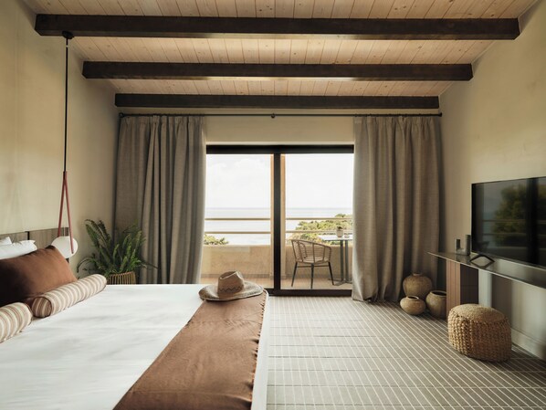 A hotel room with a bed, a TV, a balcony with a table and chairs, and a view of the sea.