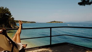 Una persona relajándose en un balcón con vistas al mar y una isla distante.