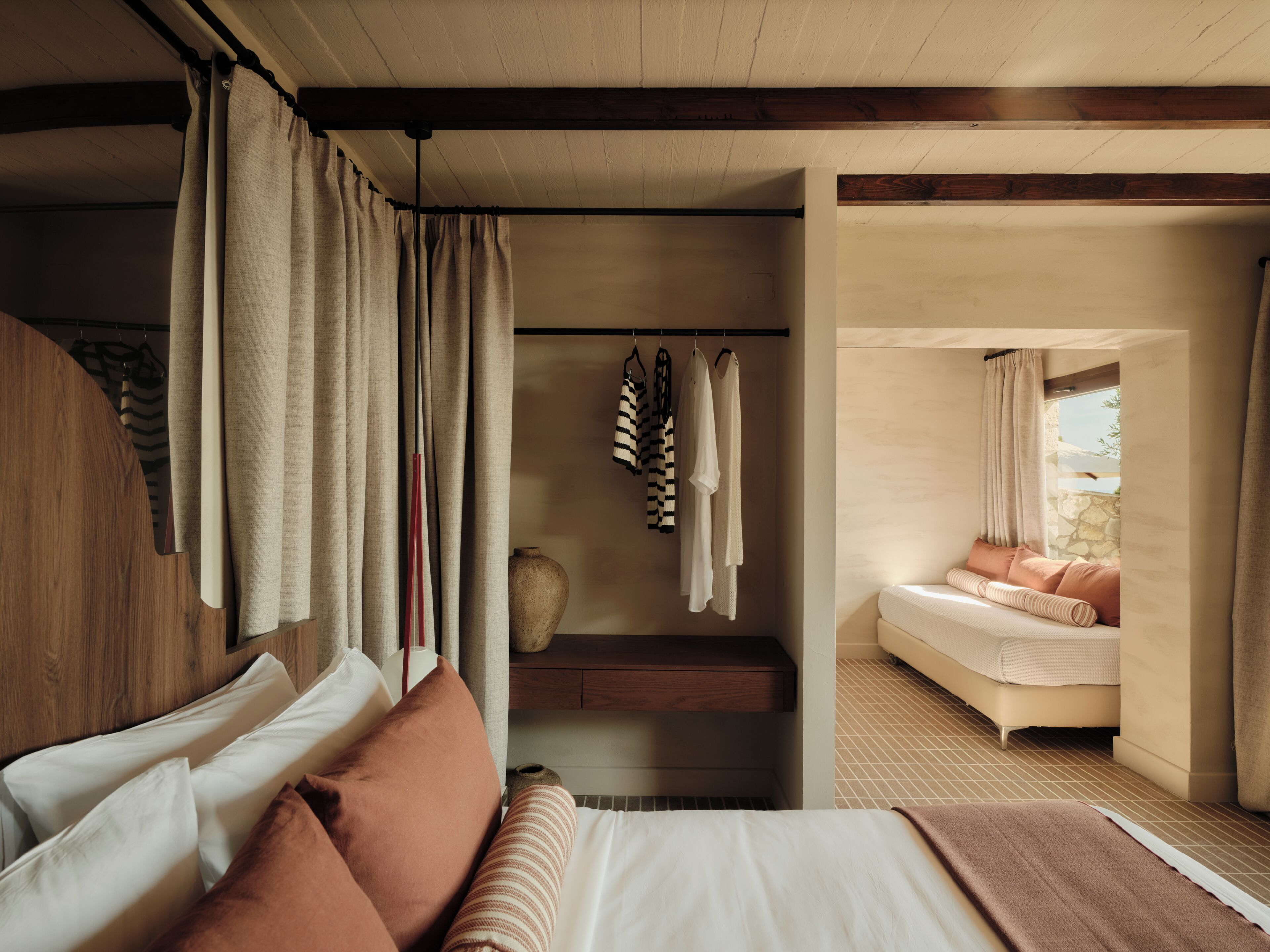Ein Schlafzimmer mit einem Bett, Kissen, einem hölzernen Kopfteil, einem Nachttisch, einer Vase und einer Kleiderstange.