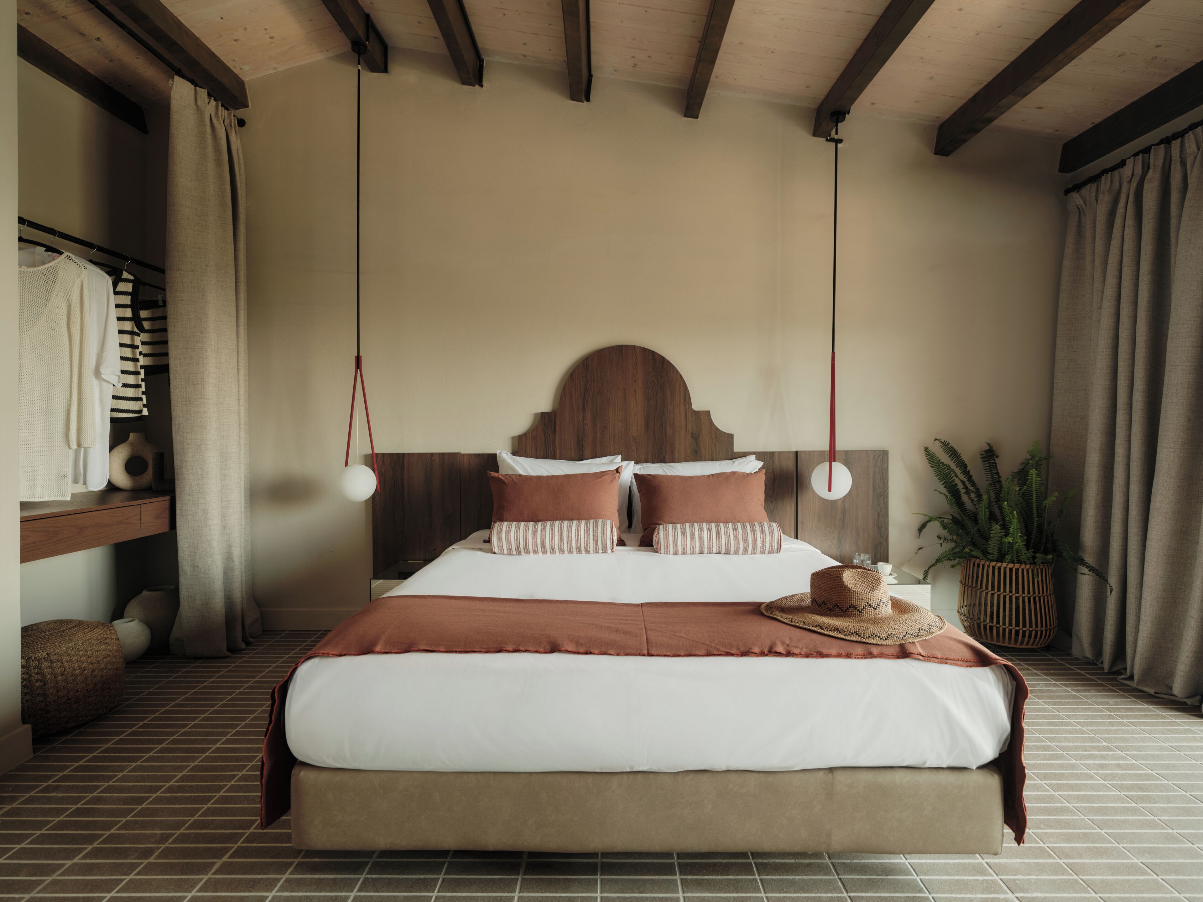 Ein ordentlich eingerichtetes Schlafzimmer mit einem großen Bett, einem Holzkopfende und einer hängenden Leuchte.