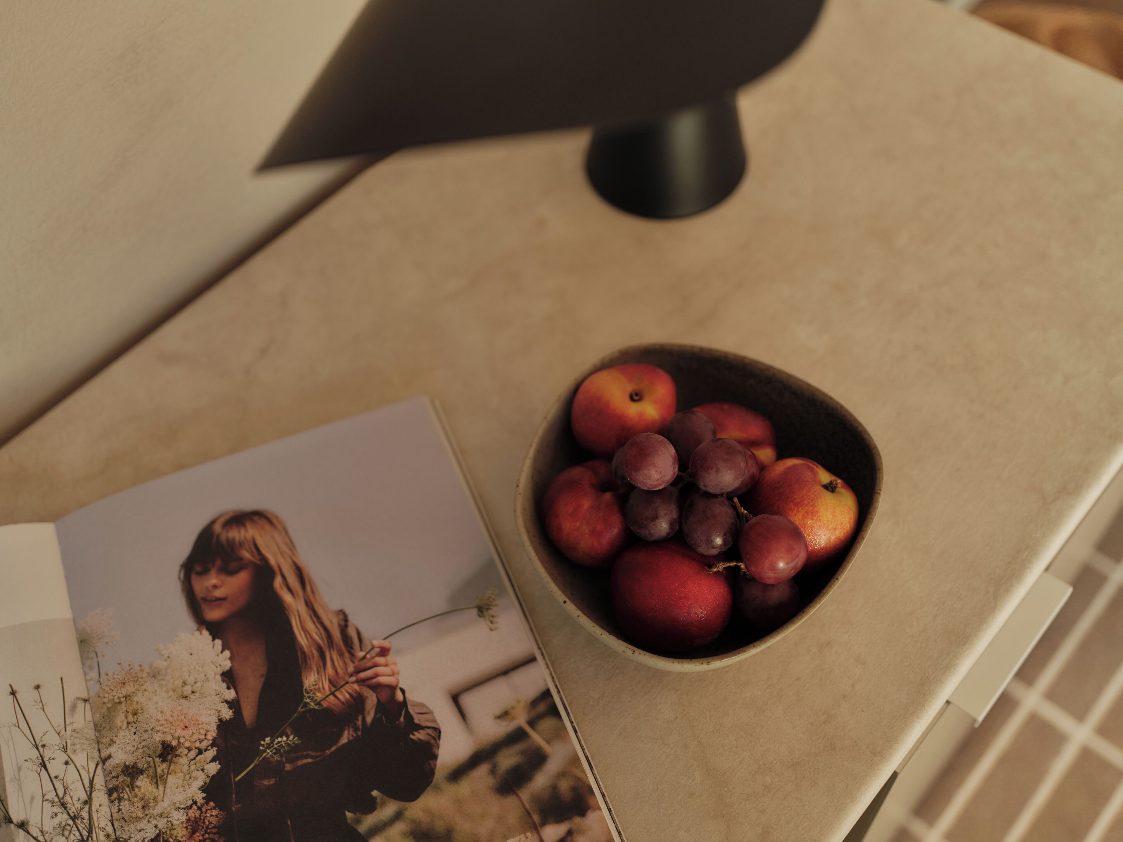 A table with a bowl of fruit, a magazine, and a lamp.