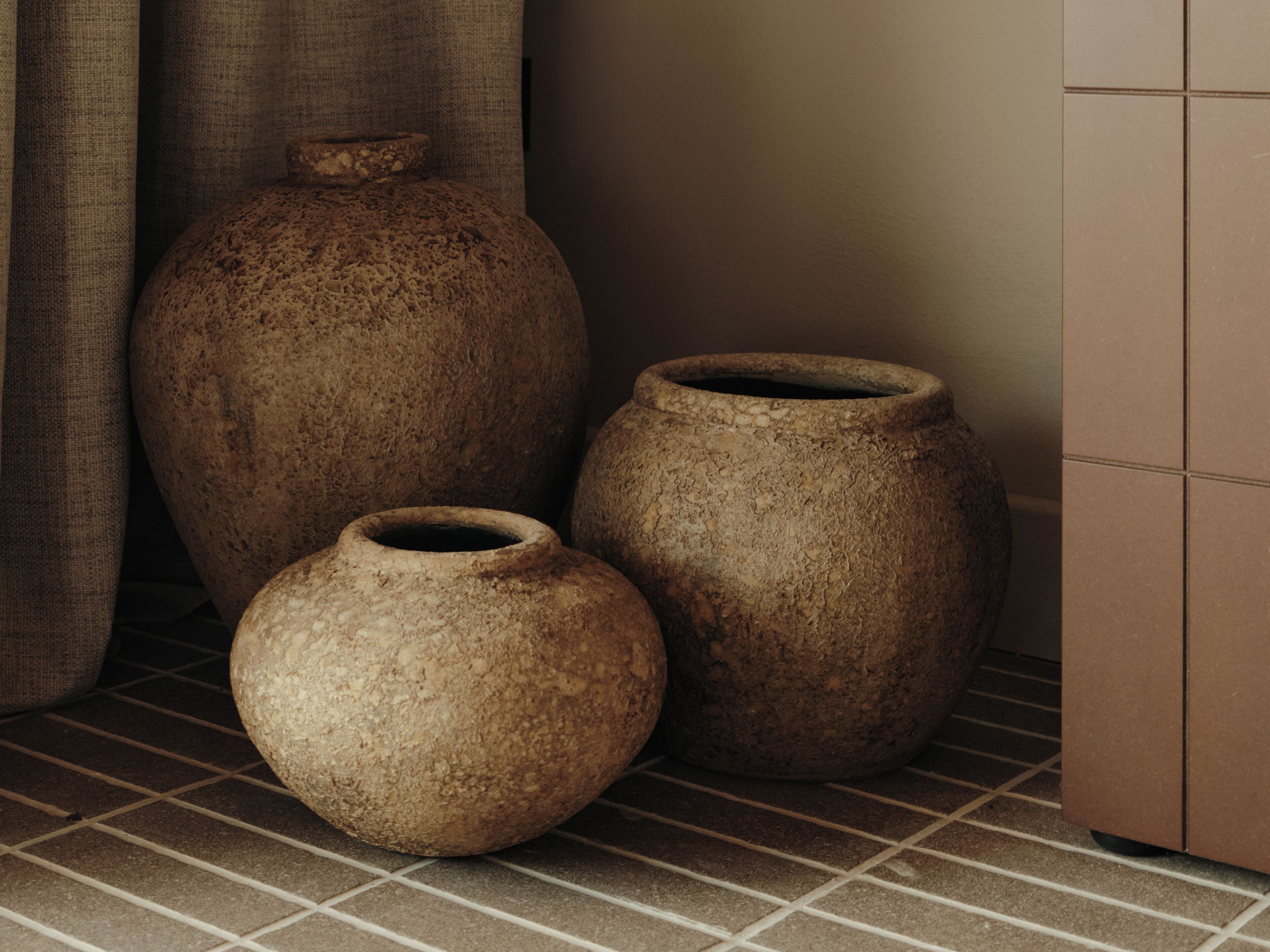 Trois vases en céramique de différentes tailles, posés sur un sol carrelé.