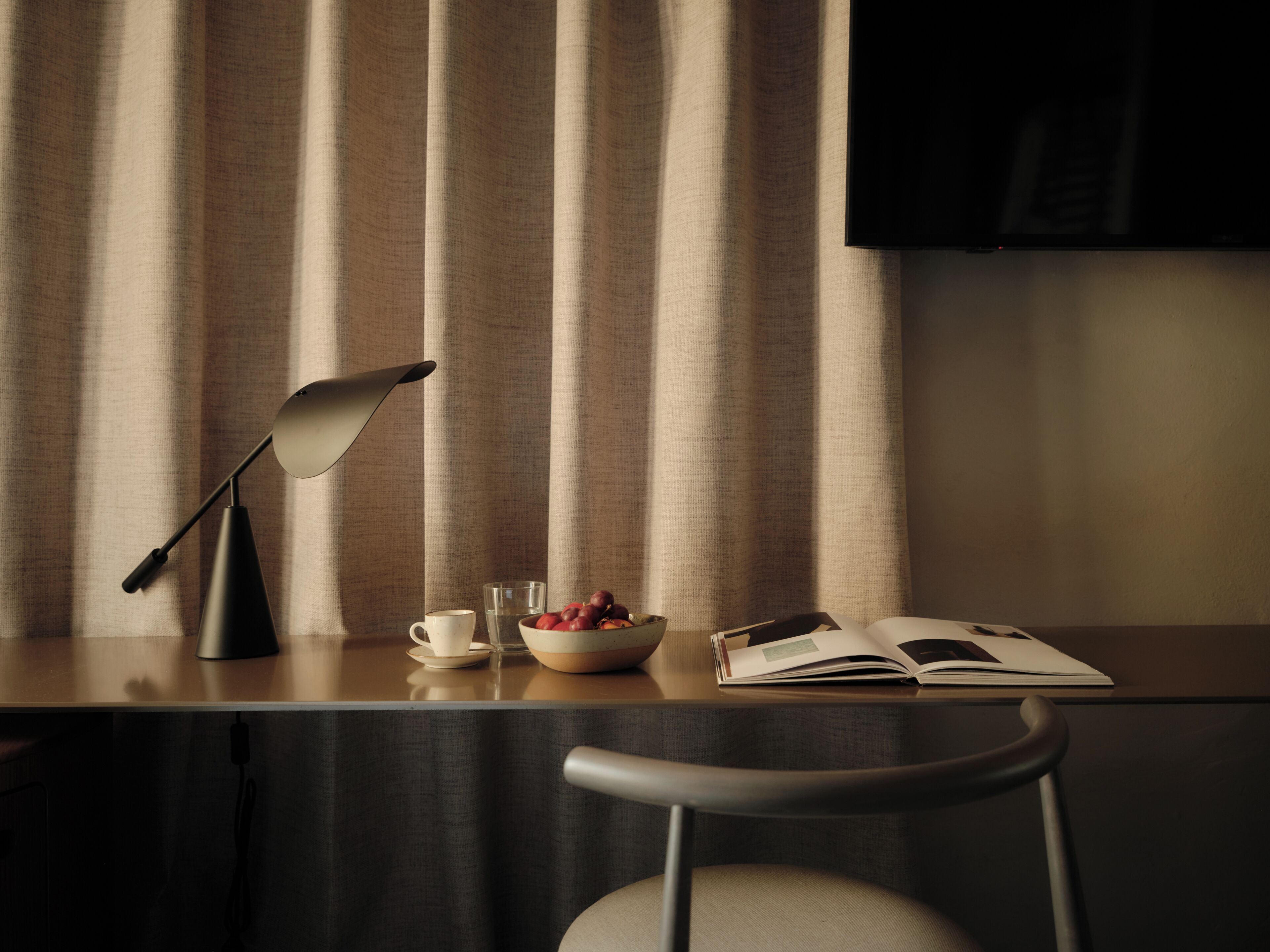 A modern room with a desk, a chair, a lamp, a bowl of fruit, a cup, and a book.