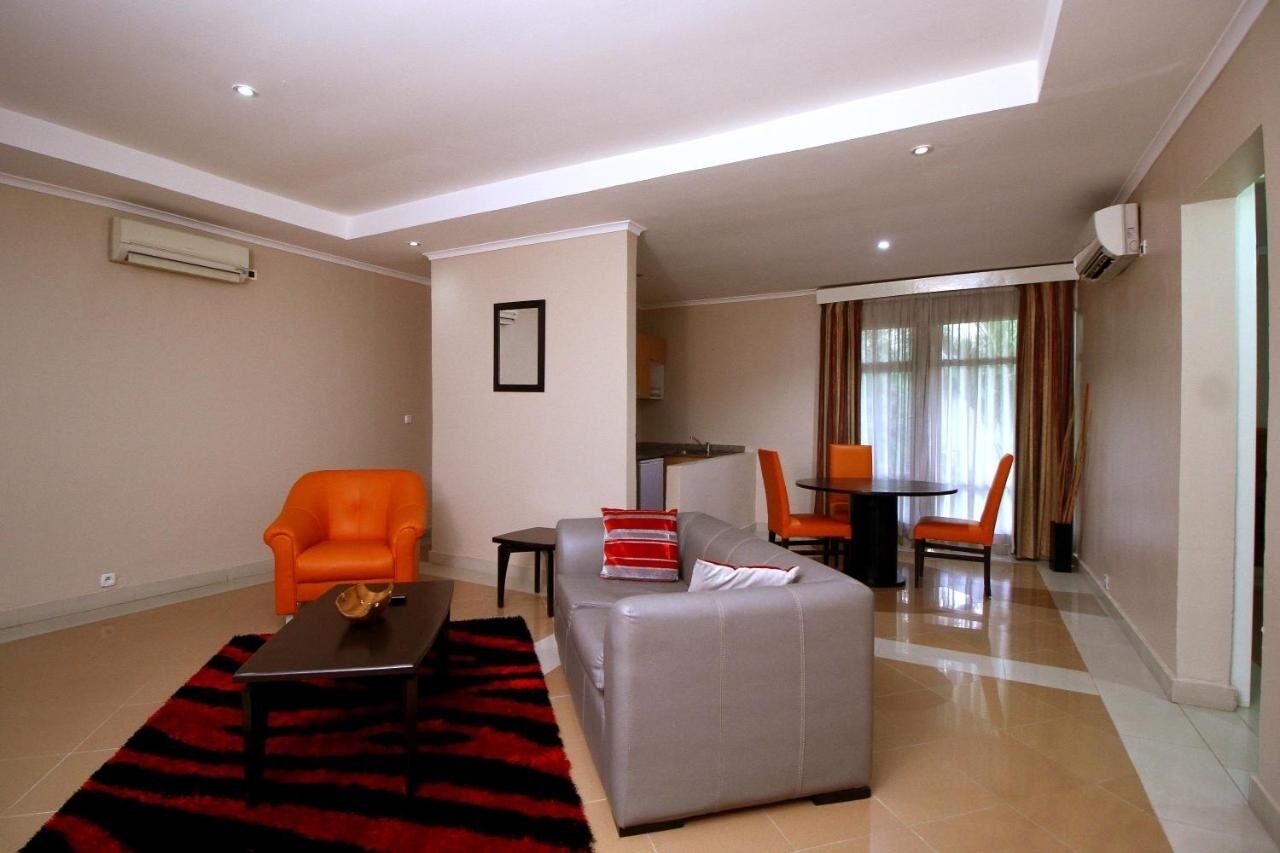 A modern living room with a grey sofa, orange armchair, and a dining area with a table and chairs.