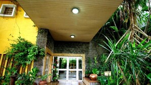 An entrance with a glass door, surrounded by potted plants and a stone wall. - La Cour - Hotels (Lagos)