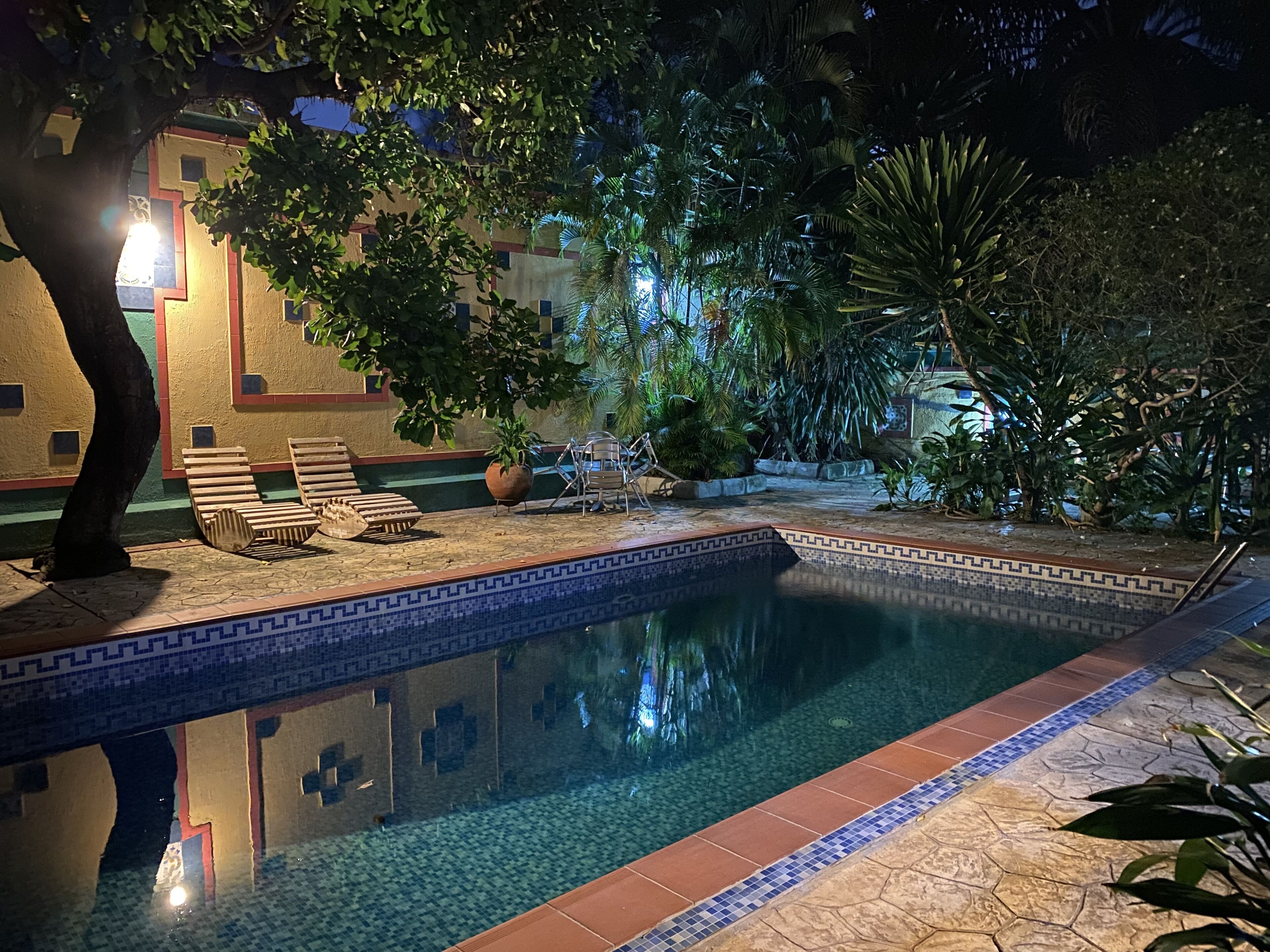 Un área de piscina nocturna con sillones de descanso y una piscina con baldosas.