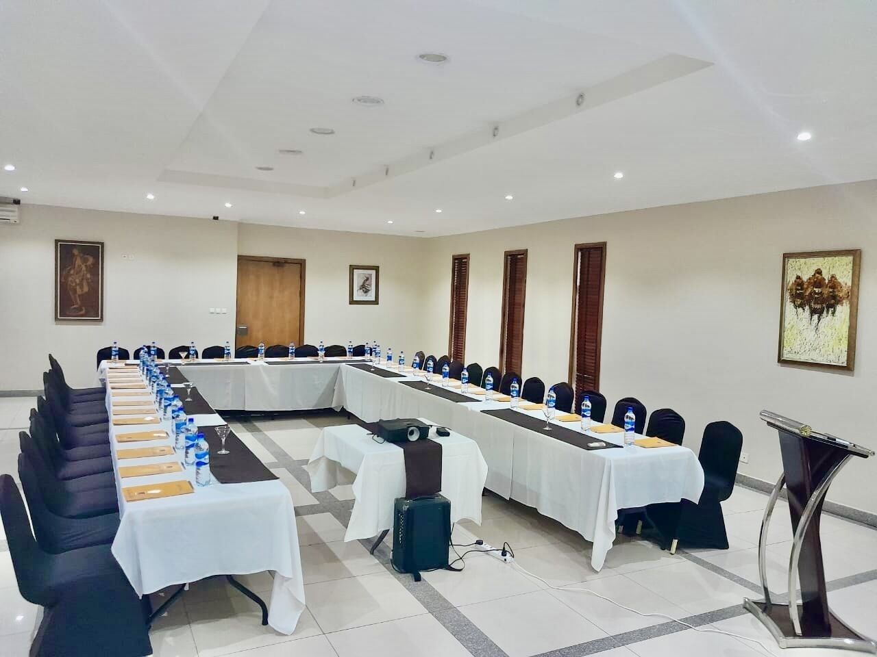 A conference room with long tables, chairs, water bottles, and a speaker.