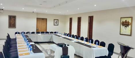 A conference room with long tables, chairs, water bottles, and a speaker.