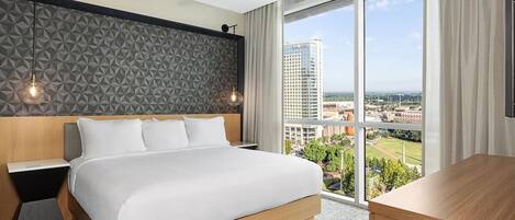 A modern hotel room with a large bed, a desk, a ceiling fan, and a city view.