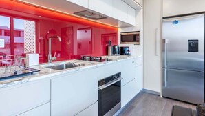 Une cuisine moderne avec des meubles blancs, un réfrigérateur en acier inoxydable et un mur d’accent rouge.