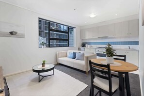 Um espaço compacto com cozinha compacta, sofá, mesa de jantar com cadeiras e uma pequena mesa lateral com uma planta.