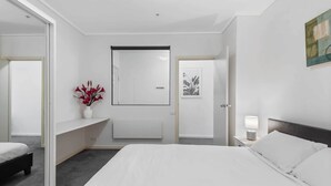 Une chambre d’hôtel moderne avec un grand lit, une table de chevet avec une lampe, un miroir et un tableau encadré au mur.
