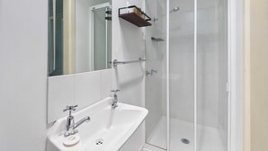 Une salle de bain avec un lavabo blanc, une cabine de douche en verre et un miroir.