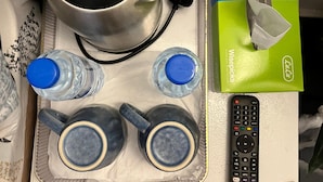 Ein Tablett mit einem Wasserkocher, zwei Wasserflaschen, zwei Tassen, einer Fernbedienung und einer Taschentuchbox.