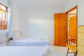 A room with two beds, a wooden wardrobe, a chair, and a window with curtains. - GB09 Ótima Casa 6 Quartos a 50m da Praia (Camaçari)