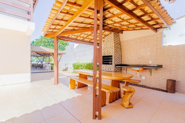 An outdoor patio with a wooden pergola, a brick oven, and a dining table with benches. - GB09 Ótima Casa 6 Quartos a 50m da Praia (Camaçari)