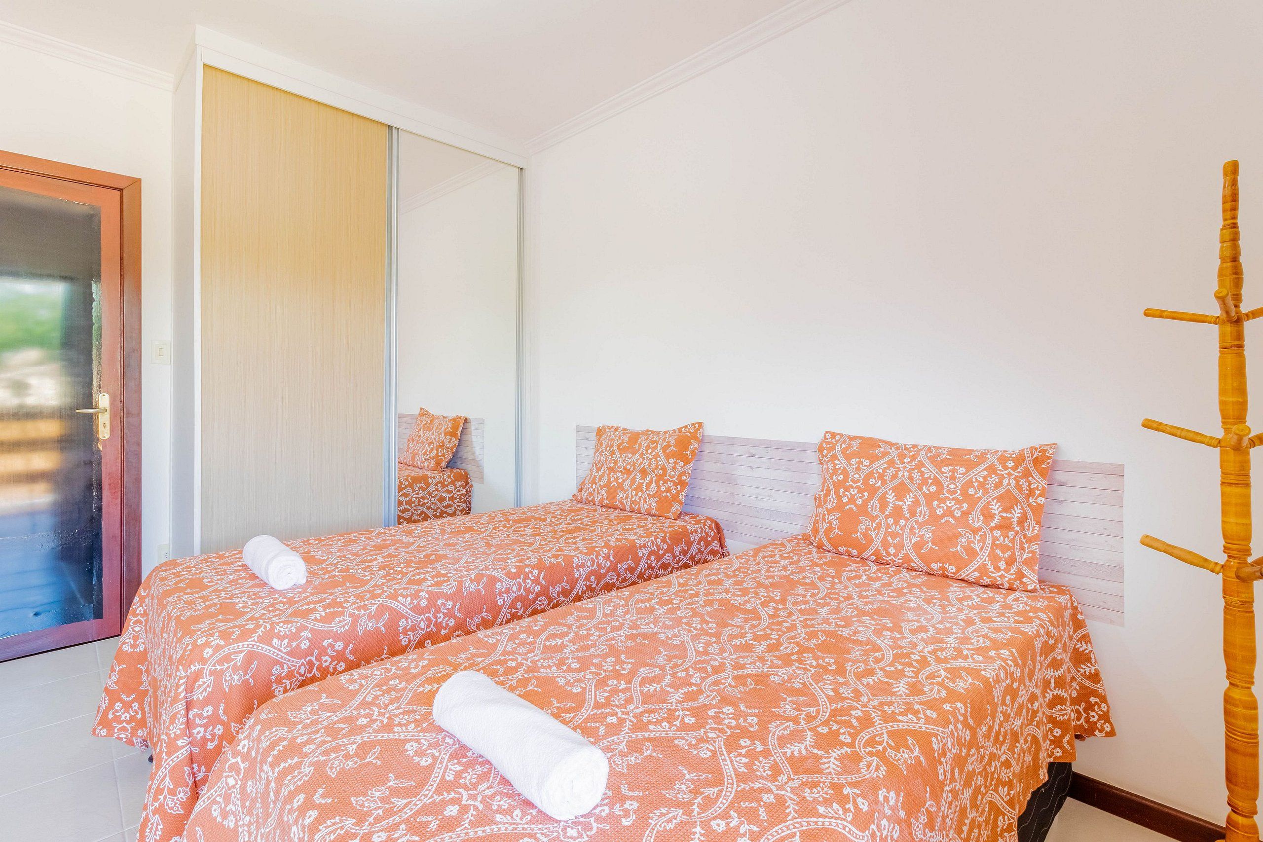 A hotel room with two beds, each with matching orange patterned bedding and white towels.