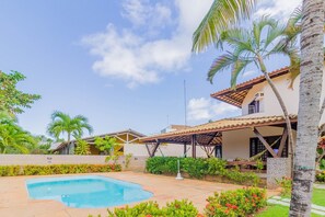 A residential area with a swimming pool, palm trees, and a house with a tiled roof. - GB09 Ótima Casa 6 Quartos a 50m da Praia (Camaçari)