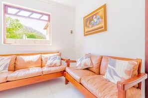 Una stanza con due divani in legno, una finestra vista verde e un quadro appeso al muro.