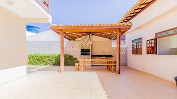 A covered patio area with a brick barbecue grill, a wooden table, and benches.