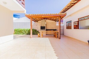 Un área de patio techada con una parrilla de ladrillo, una mesa de madera y bancos.