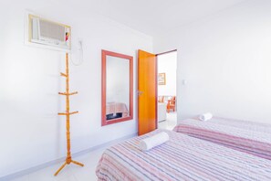 A hotel room with a bed, a bedside table, a mirror, a radiator, and a door leading to another room.