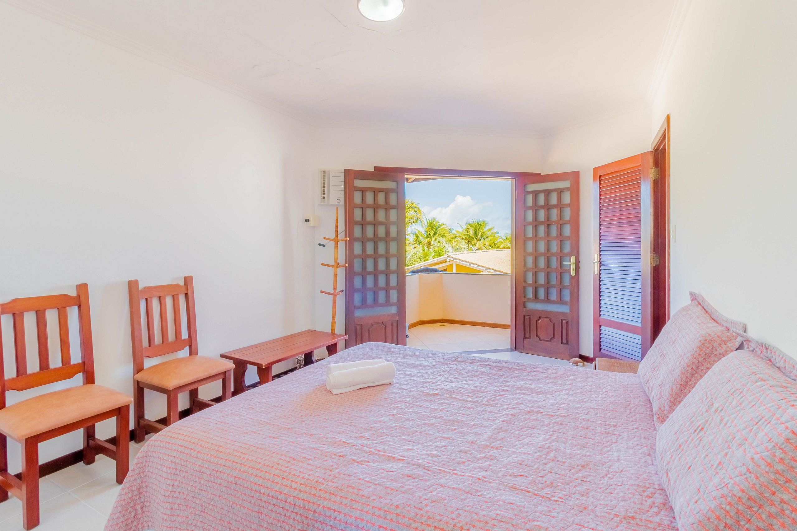 Une chambre à coucher avec un lit, deux chaises en bois, une petite table et une vue sur la plage par une porte ouverte.
