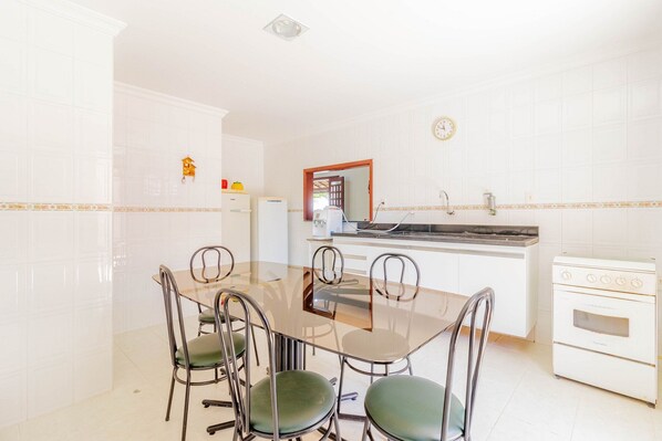A modern kitchen with a dining table, chairs, a refrigerator, a stove, and a clock on the wall.