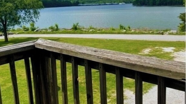 A wooden deck with a view of a lake and distant trees. - Swim, fish, and explore bluffs, just across the street. (Lowell)
