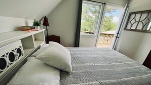 A bedroom with a bed, pillows, a nightstand, a lamp, a window, and a view of the outdoors. - Swim, fish, and explore bluffs, just across the street. (Lowell)