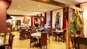A restaurant with wooden beams, red curtains, and a central dining area with round tables and chairs. - Speicher-studio 3 (Klein Upahl)