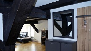A room with exposed wooden beams, a black sofa, a wooden cabinet, and a mirror on the wall. - Speicher-studio 3 (Klein Upahl)