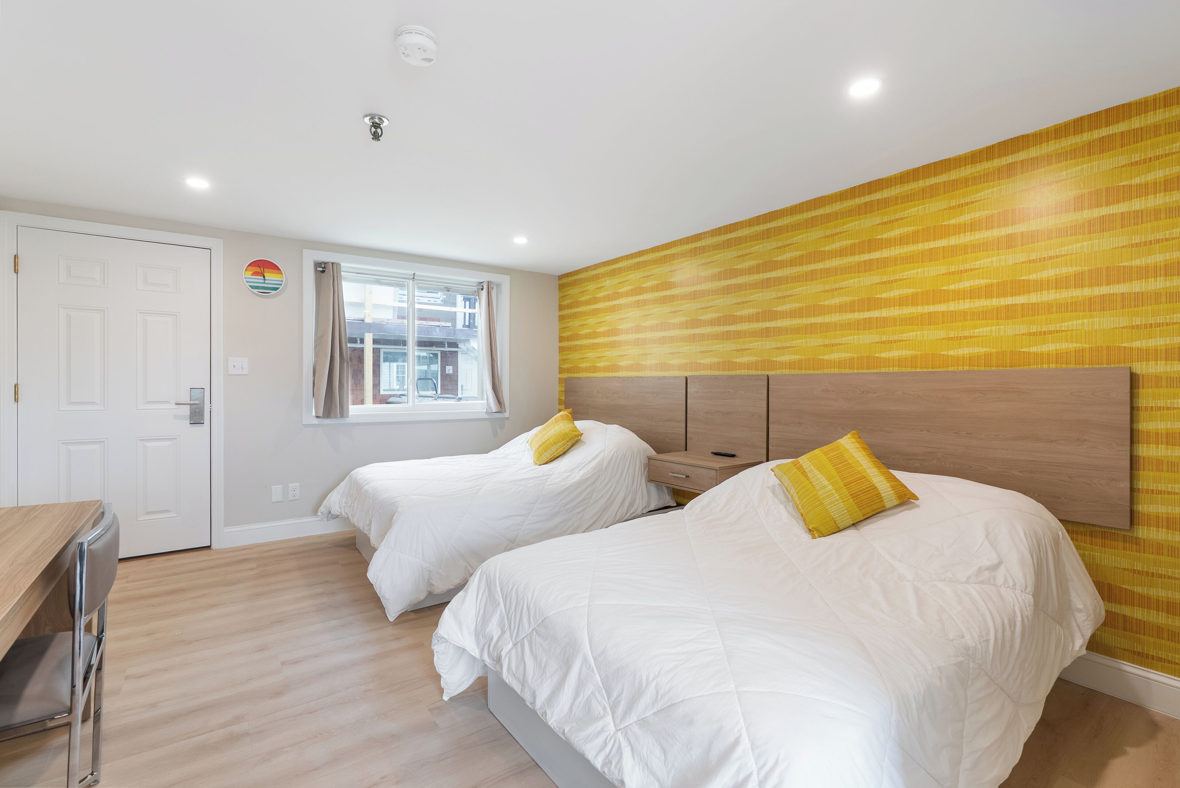 Une chambre avec deux lits, un bureau en bois et une fenêtre avec des rideaux.