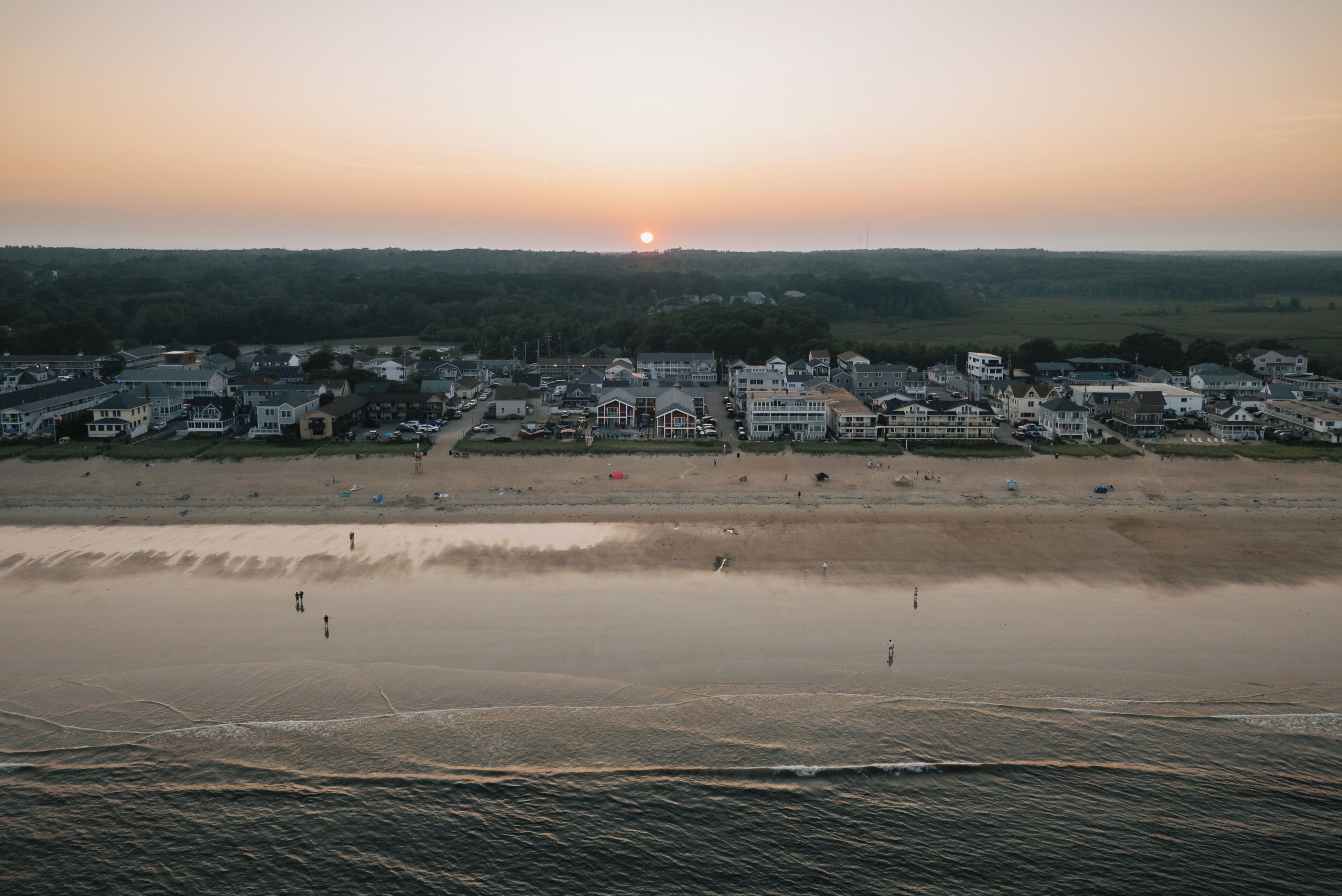 Een kustplaatsje met woongebouwen, een strand en een ondergaande zon.